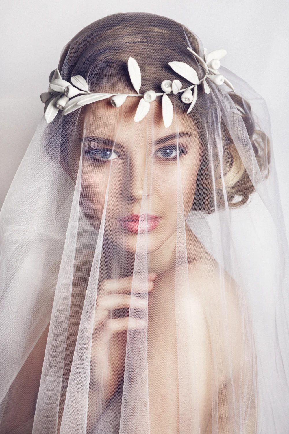 Model wearing a veil over the face with a flower crown hair accessory.