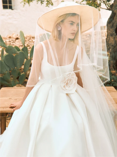 Model wearing a wedding dress with a veil attached to a hat